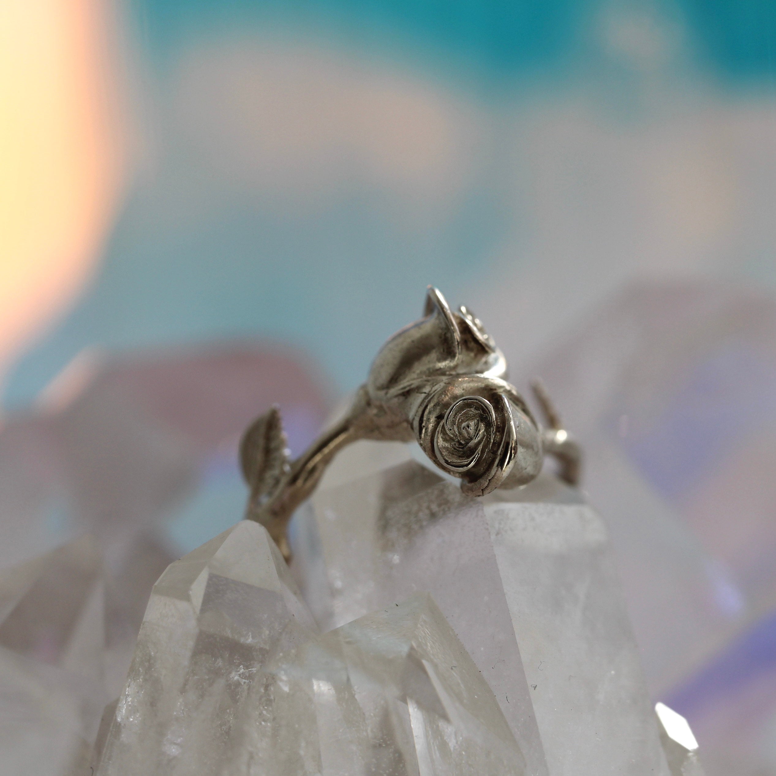 A sterling silver ring with a textured design featuring two wild roses and petals, displayed on a crystal.