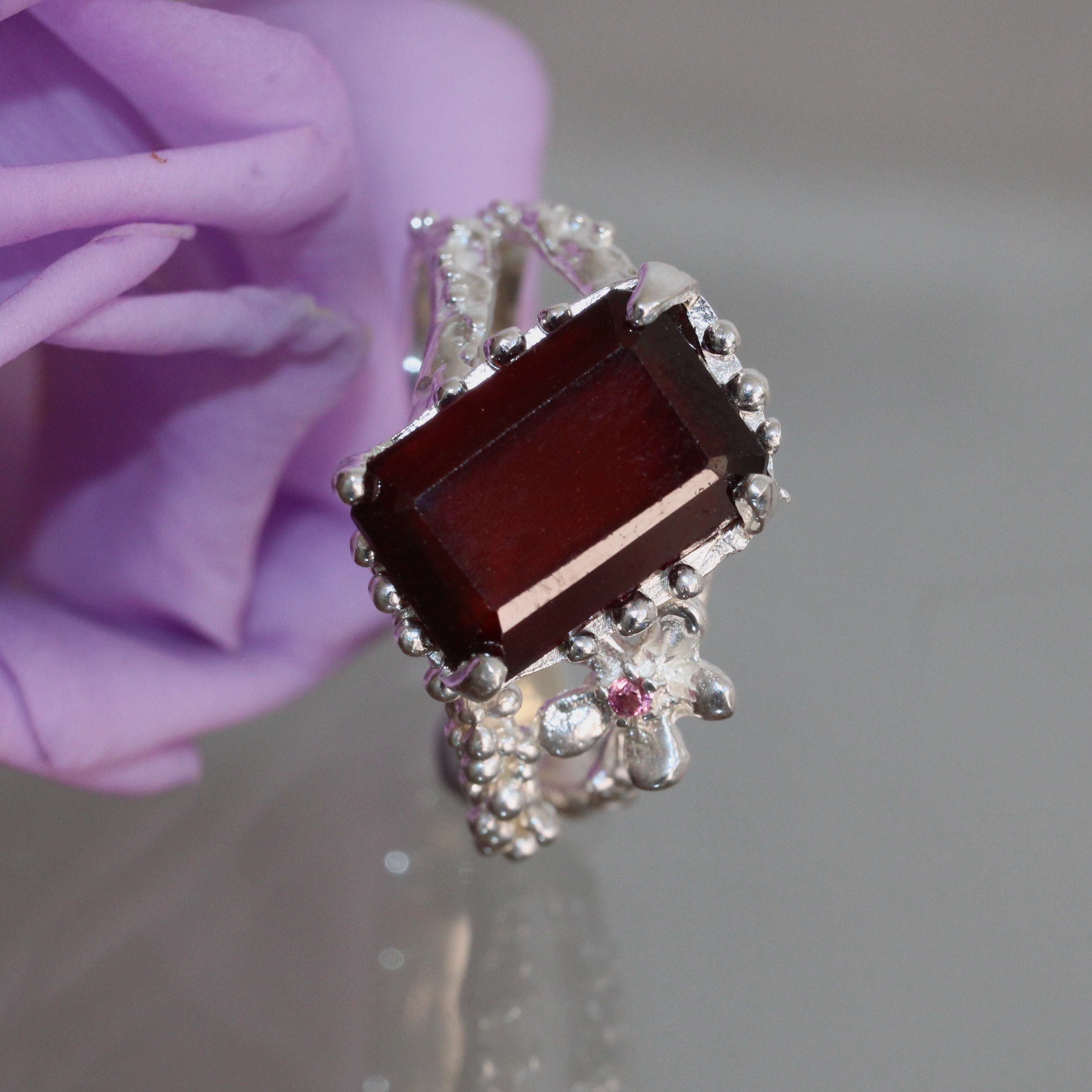 Silver ring with a large red gemstone near purple flower