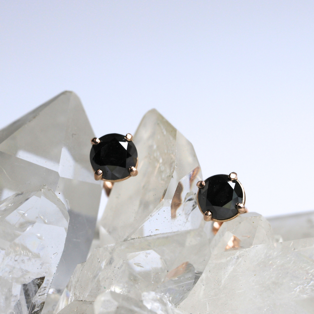 A pair of black diamond studs set in a silver mounting, displayed against a crystal background.