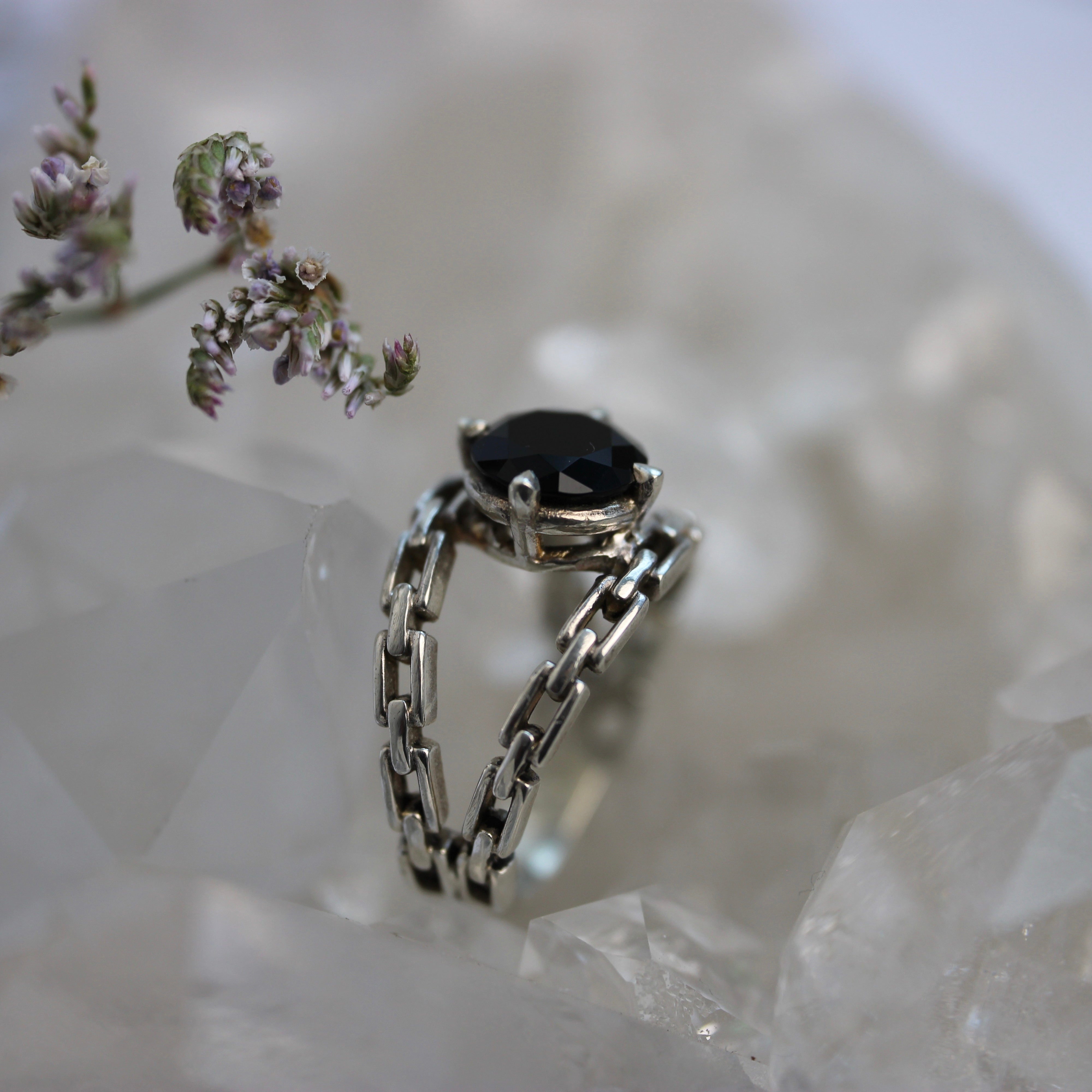 Silver chain ring with a black gemstone on a crystal surface