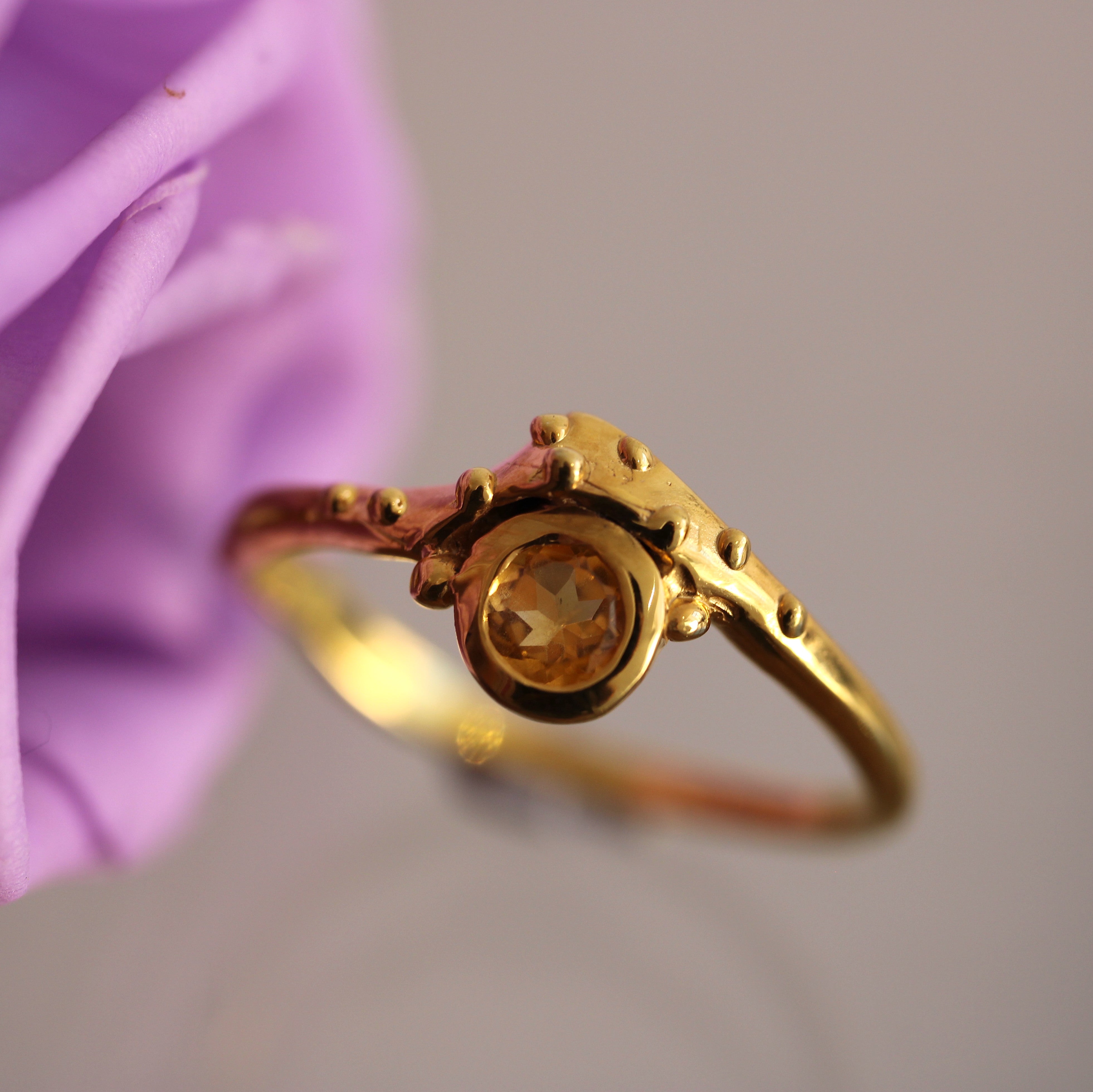 Gold ring with a gemstone in front of a purple flower