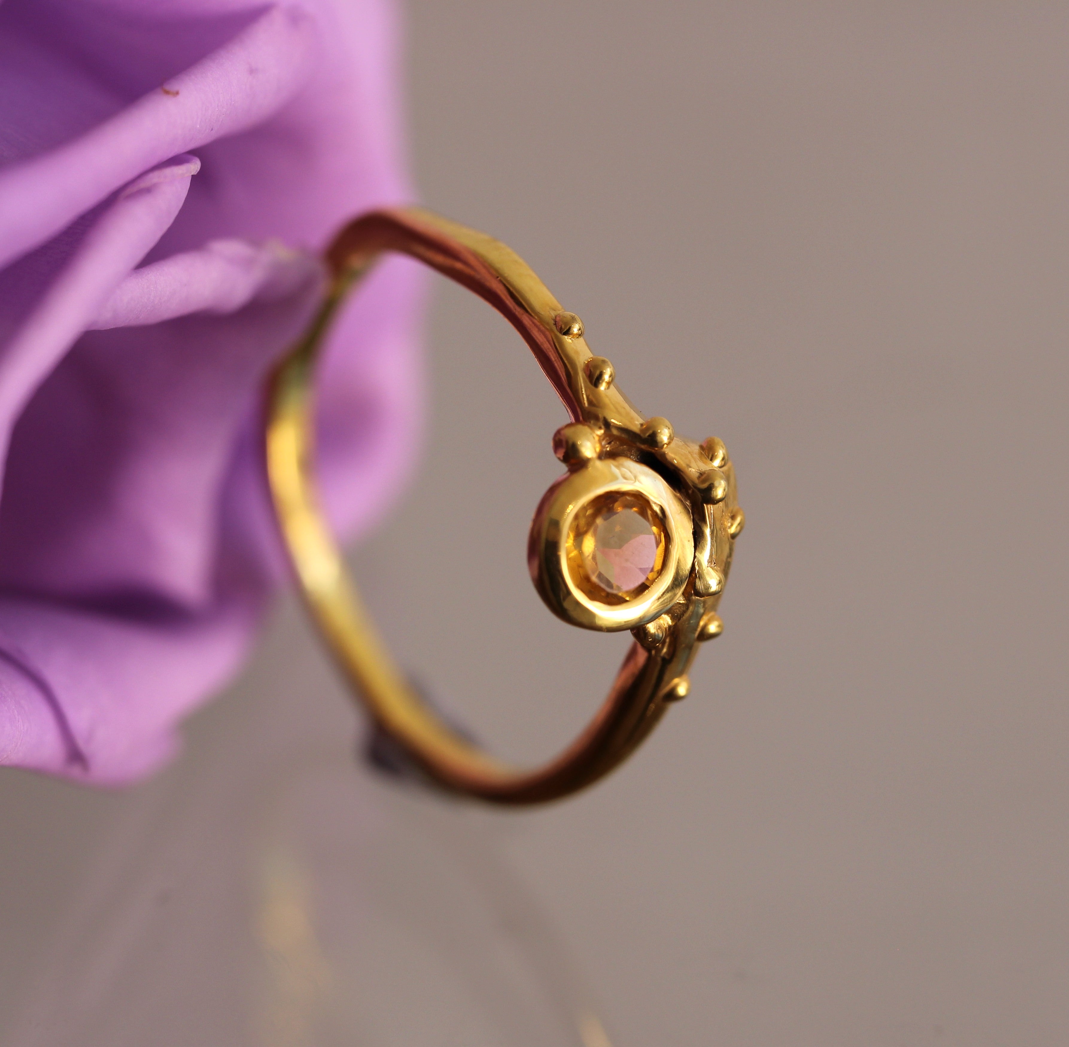 Gold ring with a gemstone held against a purple flower