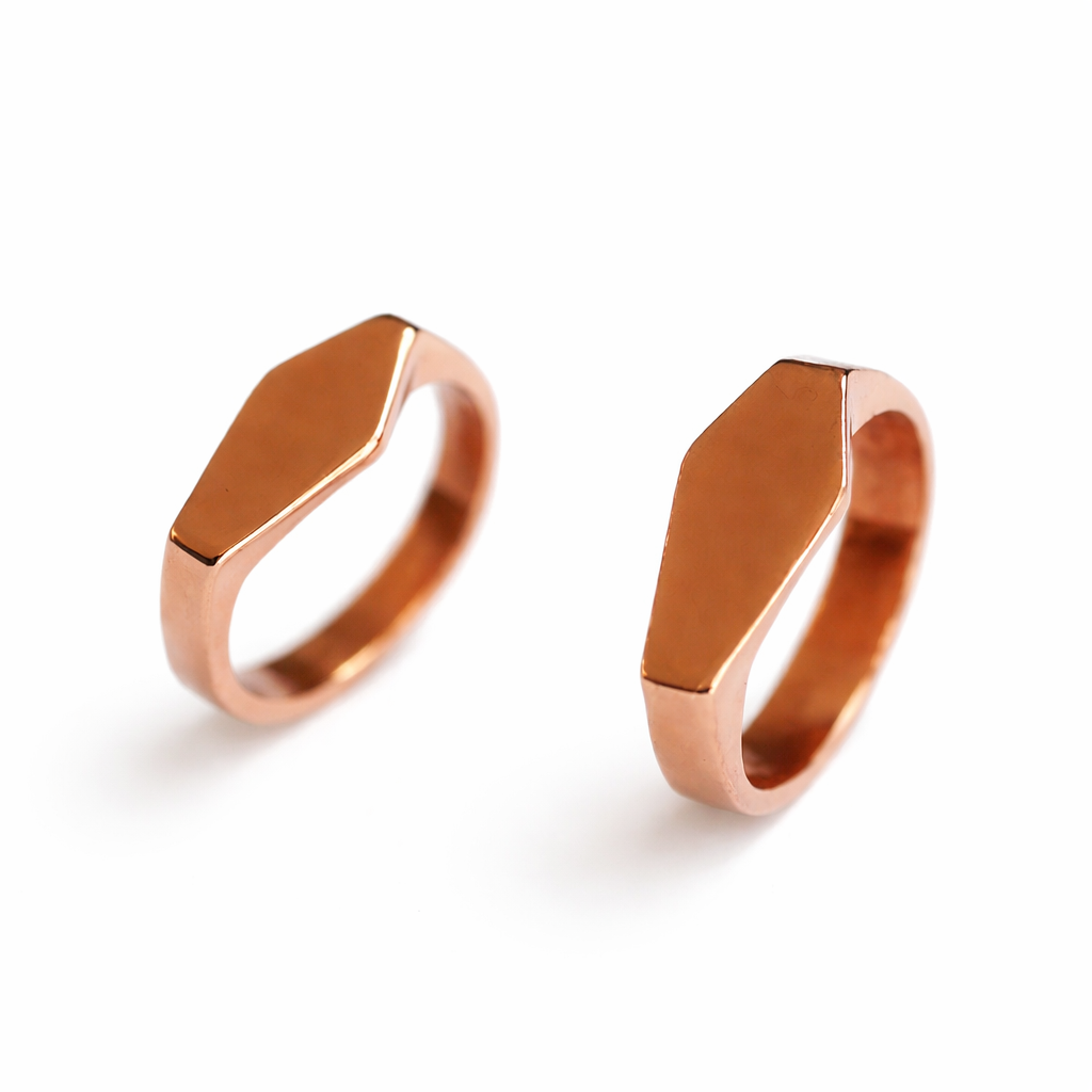 Two rose gold rings in the shape of a coffin on a white background