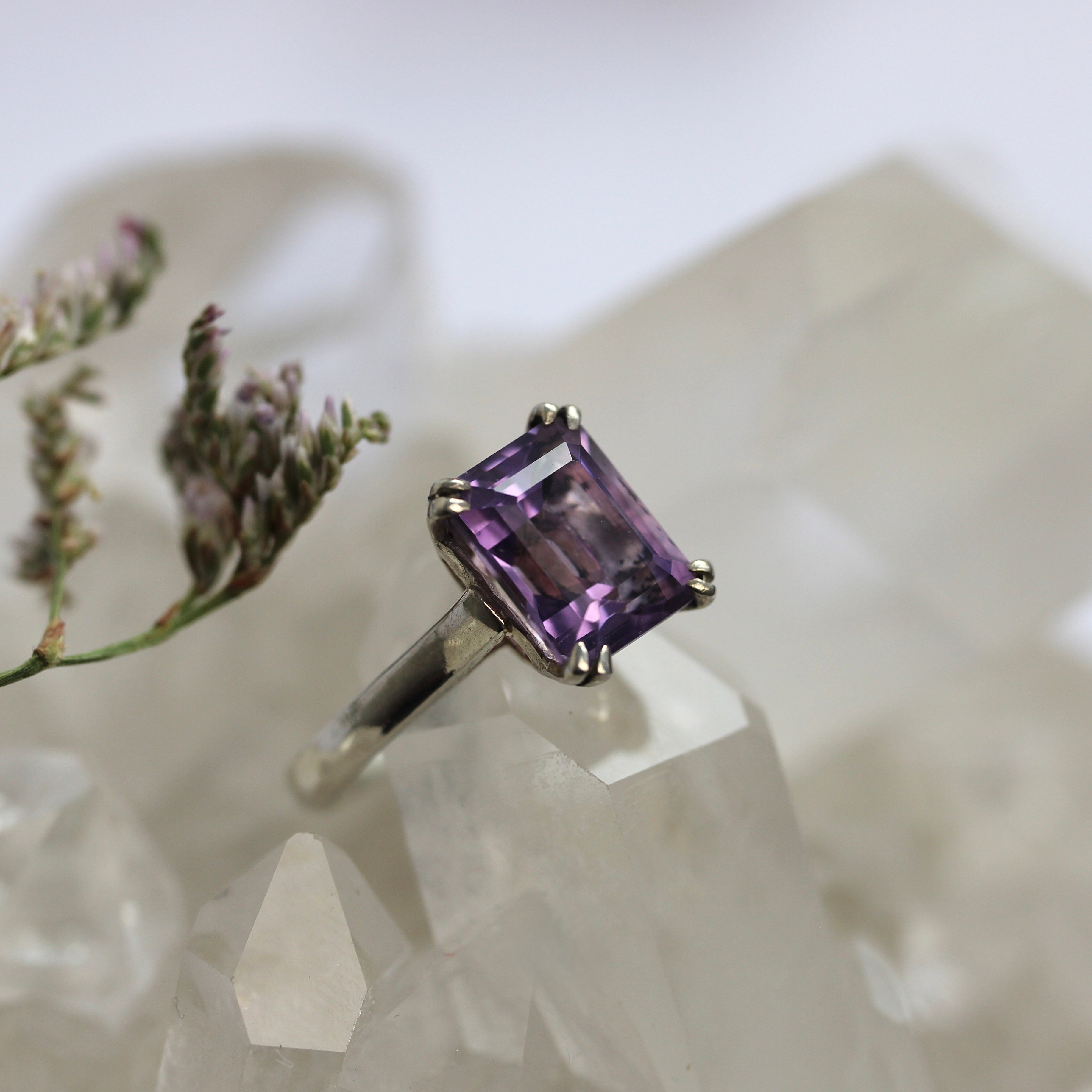 Ring with a purple gemstone on a marble surface with lavender flowers.