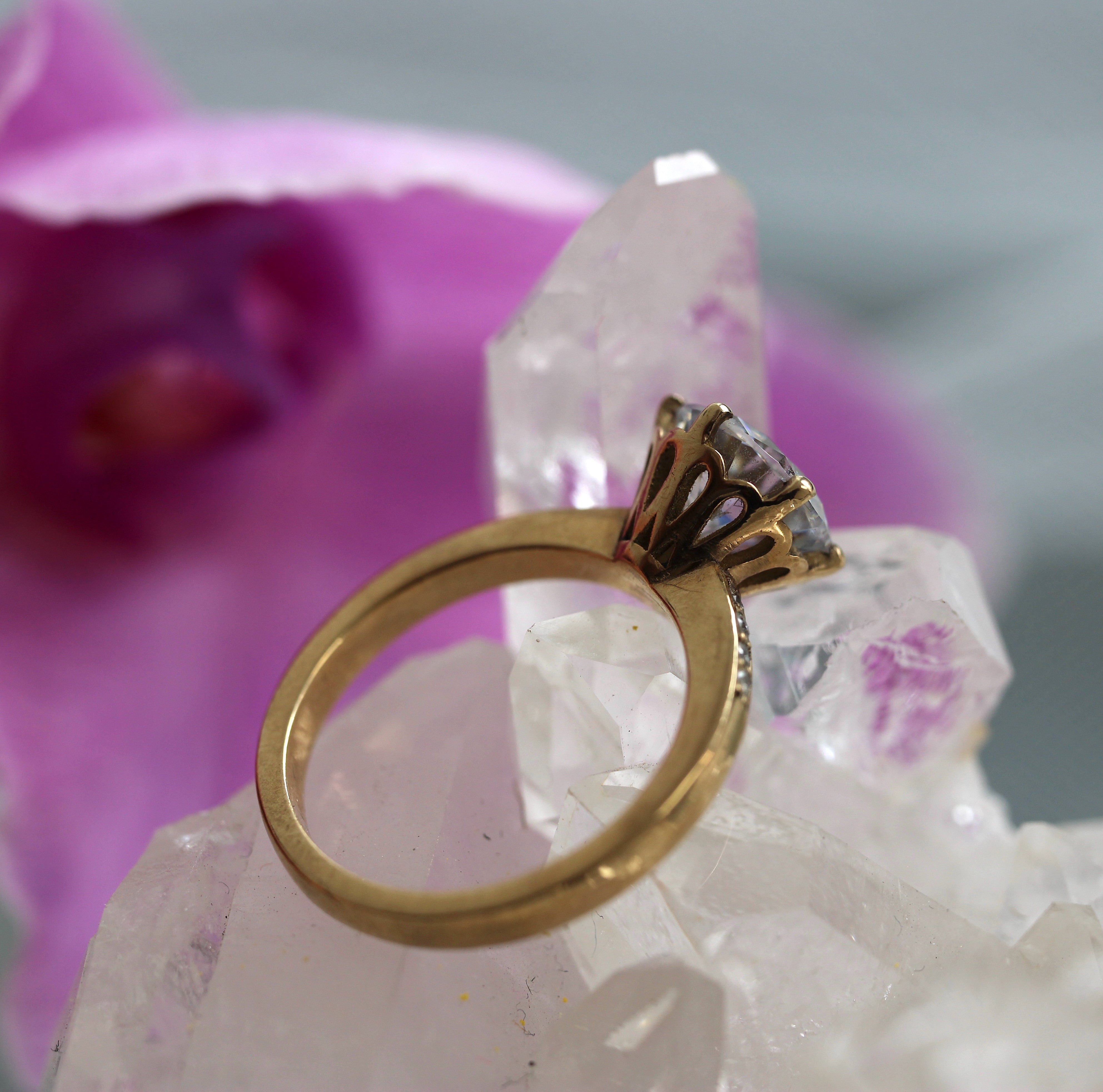 Gold ring with a decorative setting on a crystal with pink orchid in the background