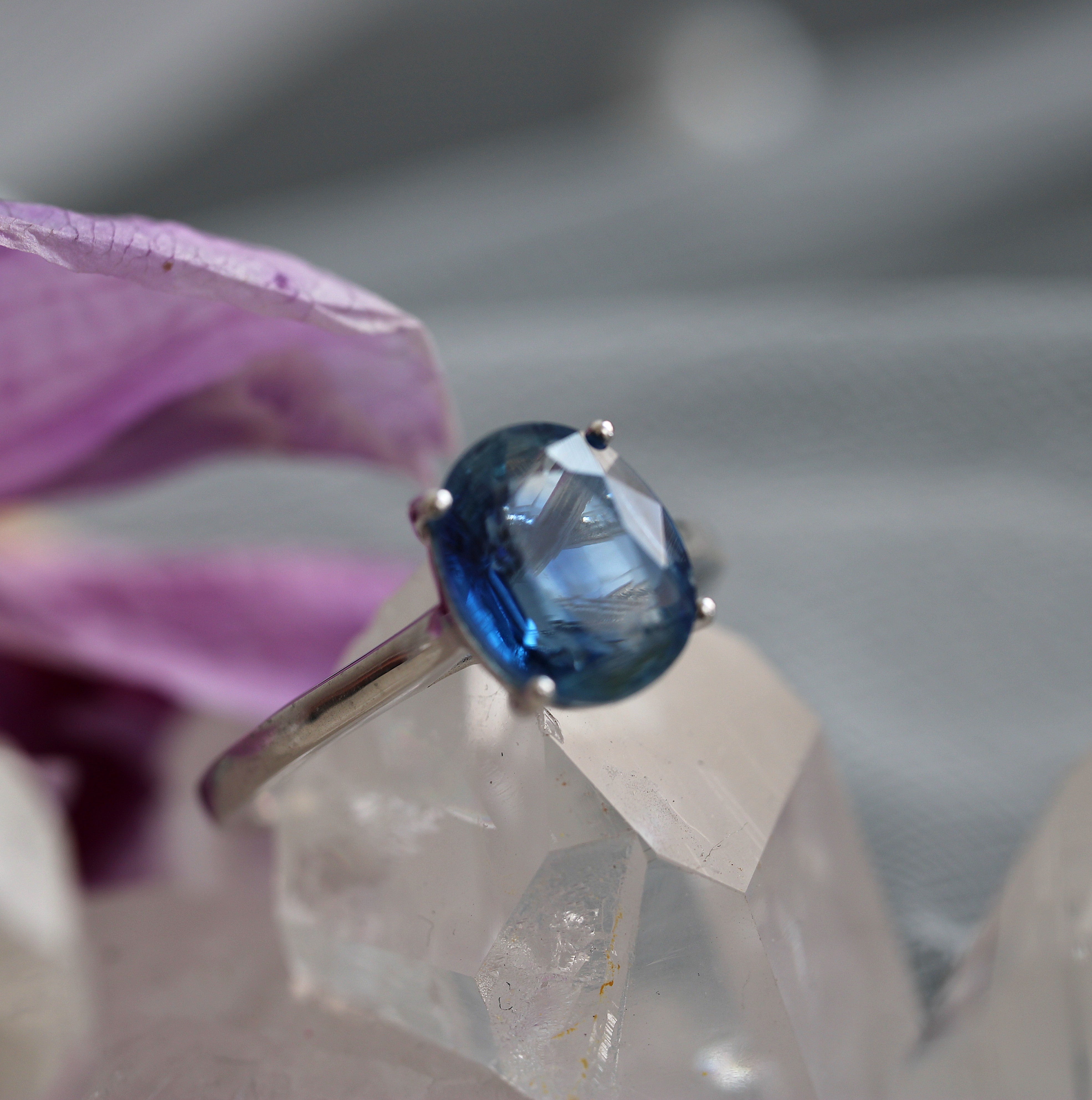 Ring with a blue kyanite held over a crystal and purple flower