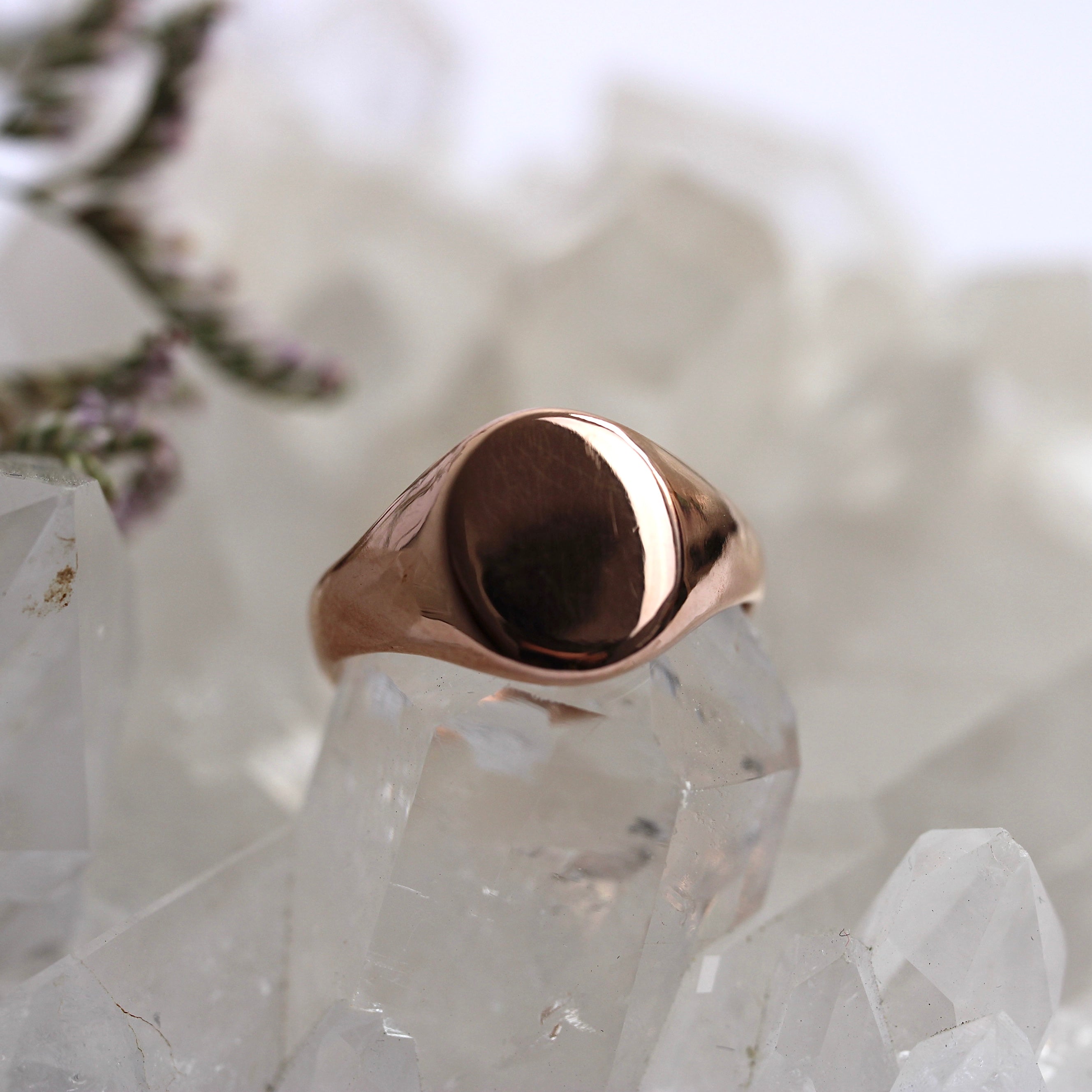 Rose gold signet ring on a clear crystal with a blurred natural background