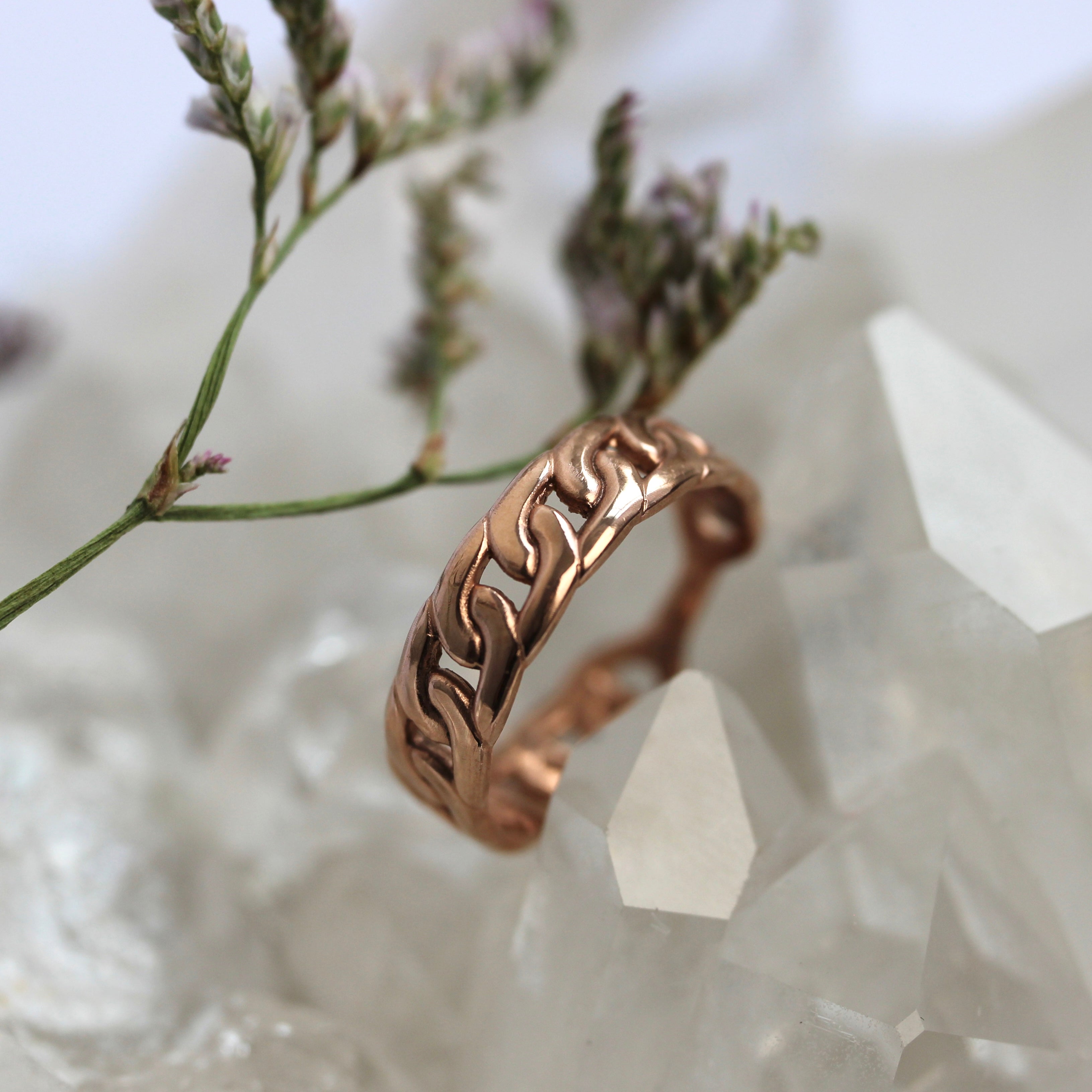Rose gold ring with intricate design on a crystal and plant background