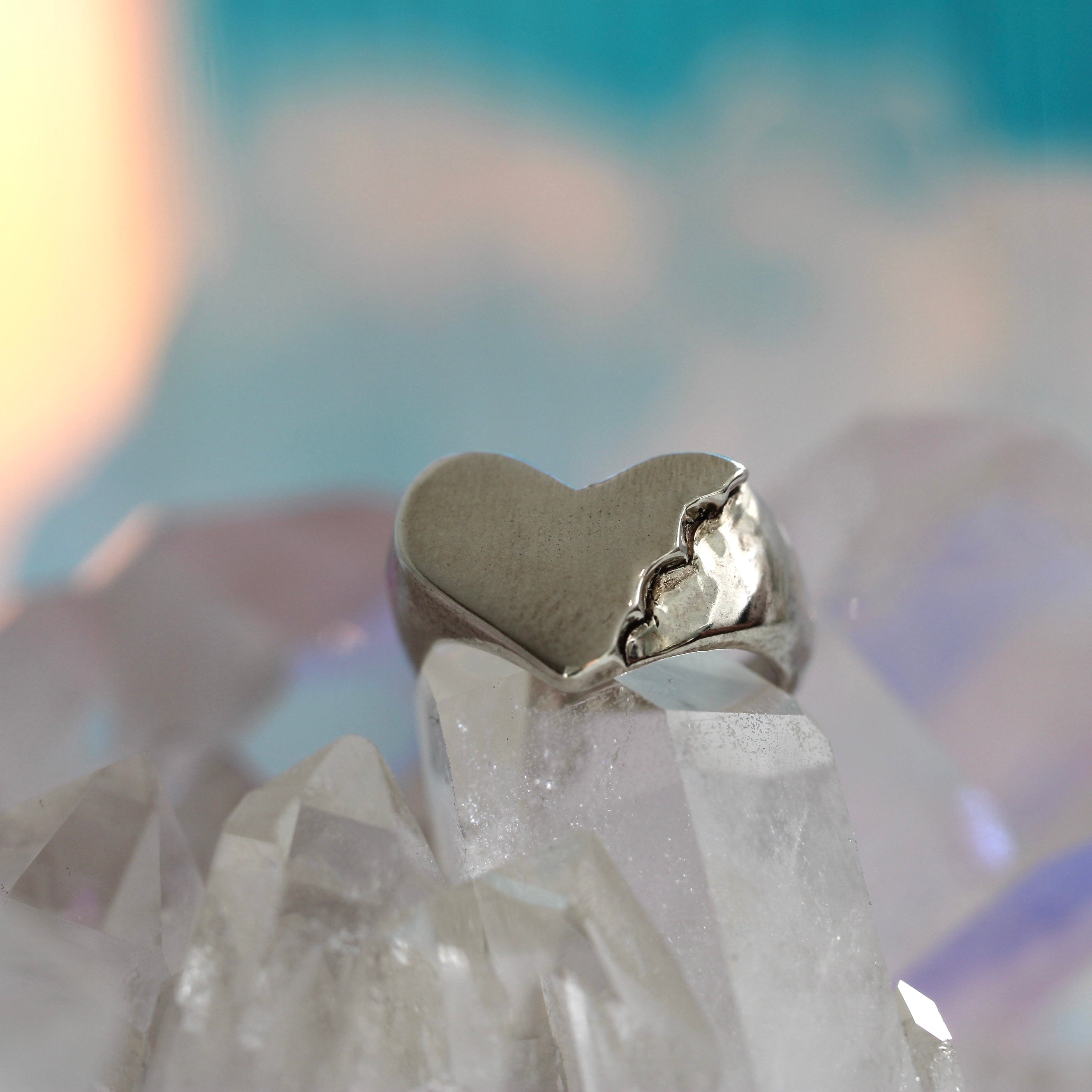 A silver heart-shaped signet ring with a bite mark texture on a crystal.