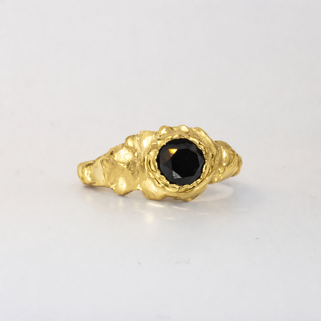 Gold ring with a black gemstone on a light gray background