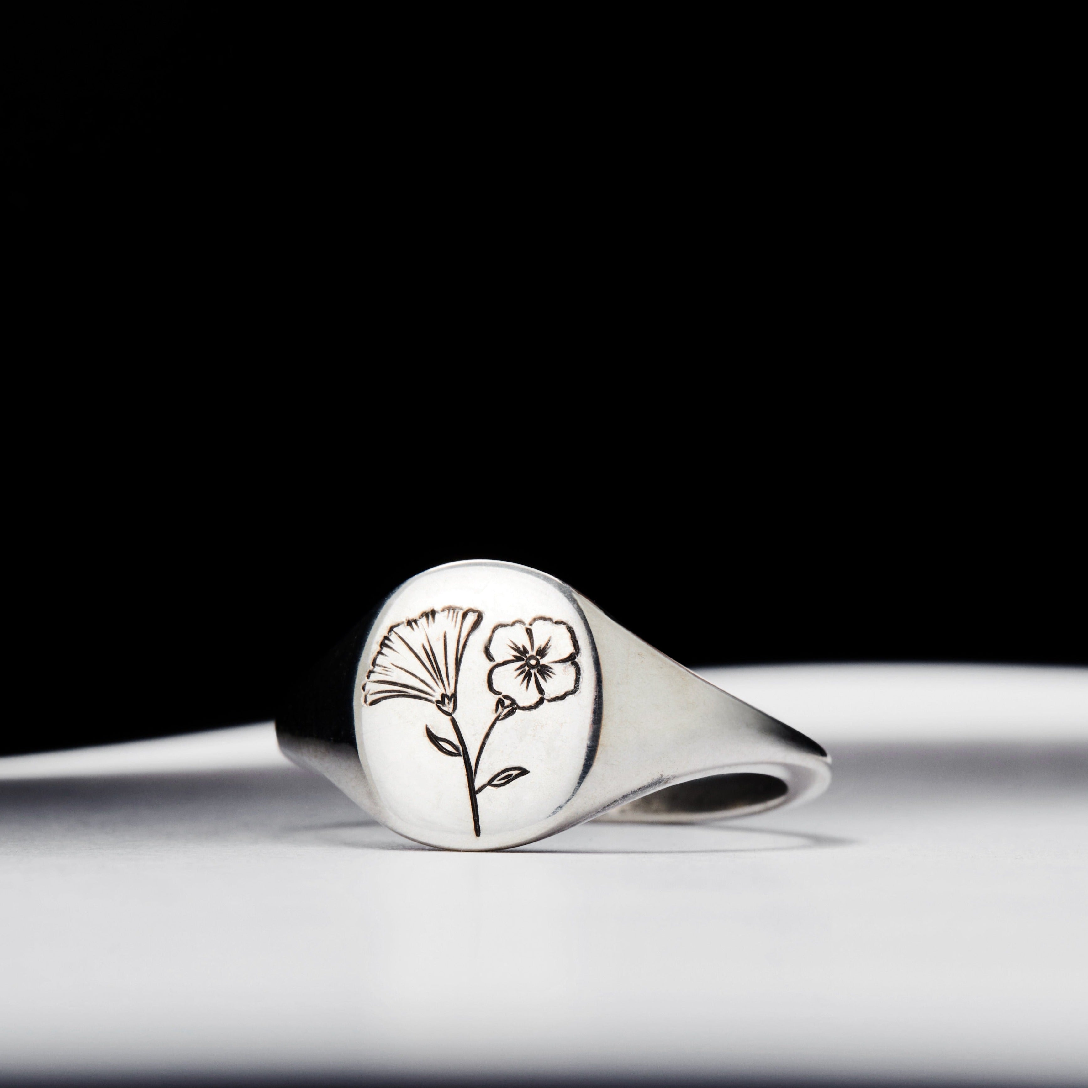 A silver signet ring with a floral design on a white background.
