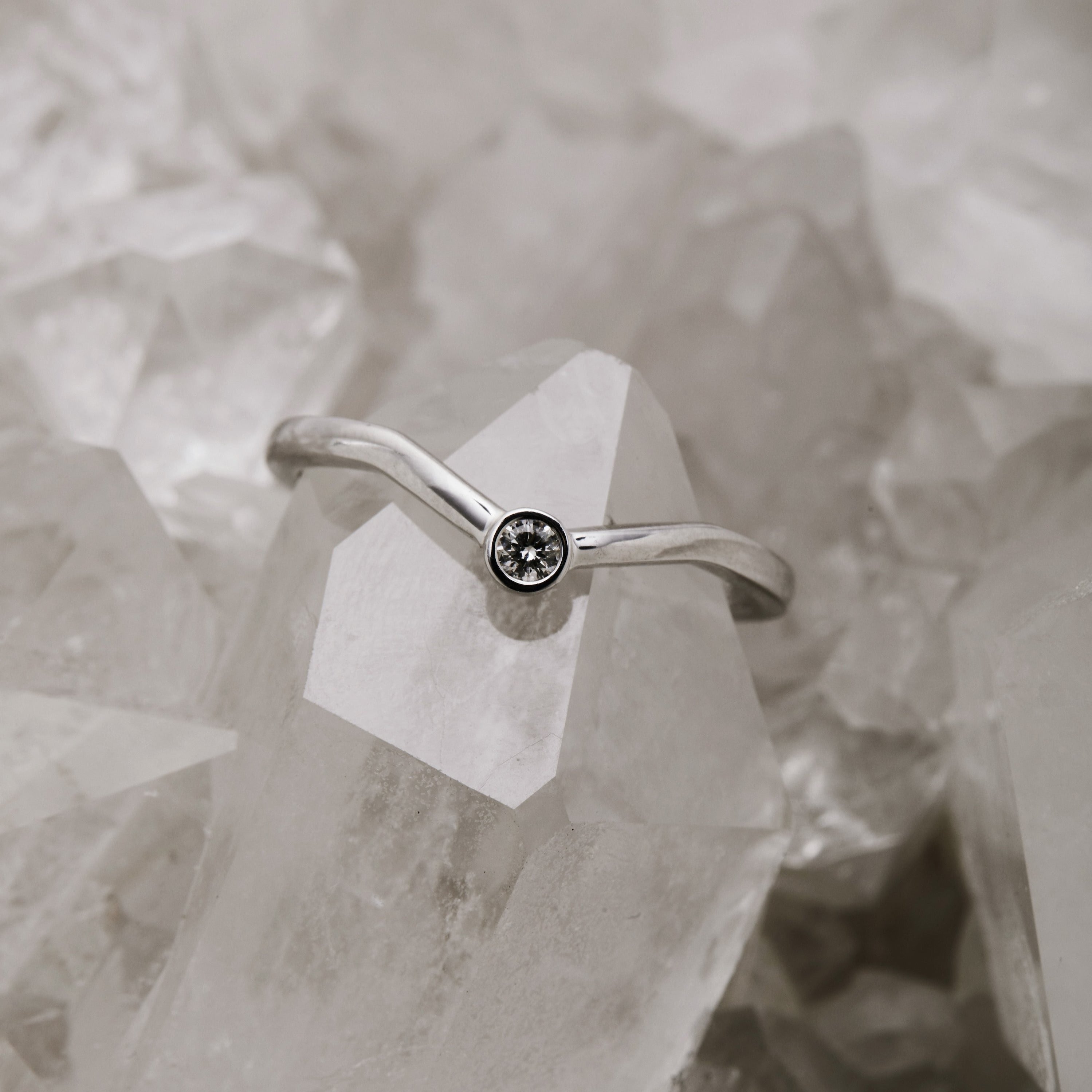 A silver stacker ring with a chevron design featuring a central round diamond, displayed on a crystal surface.