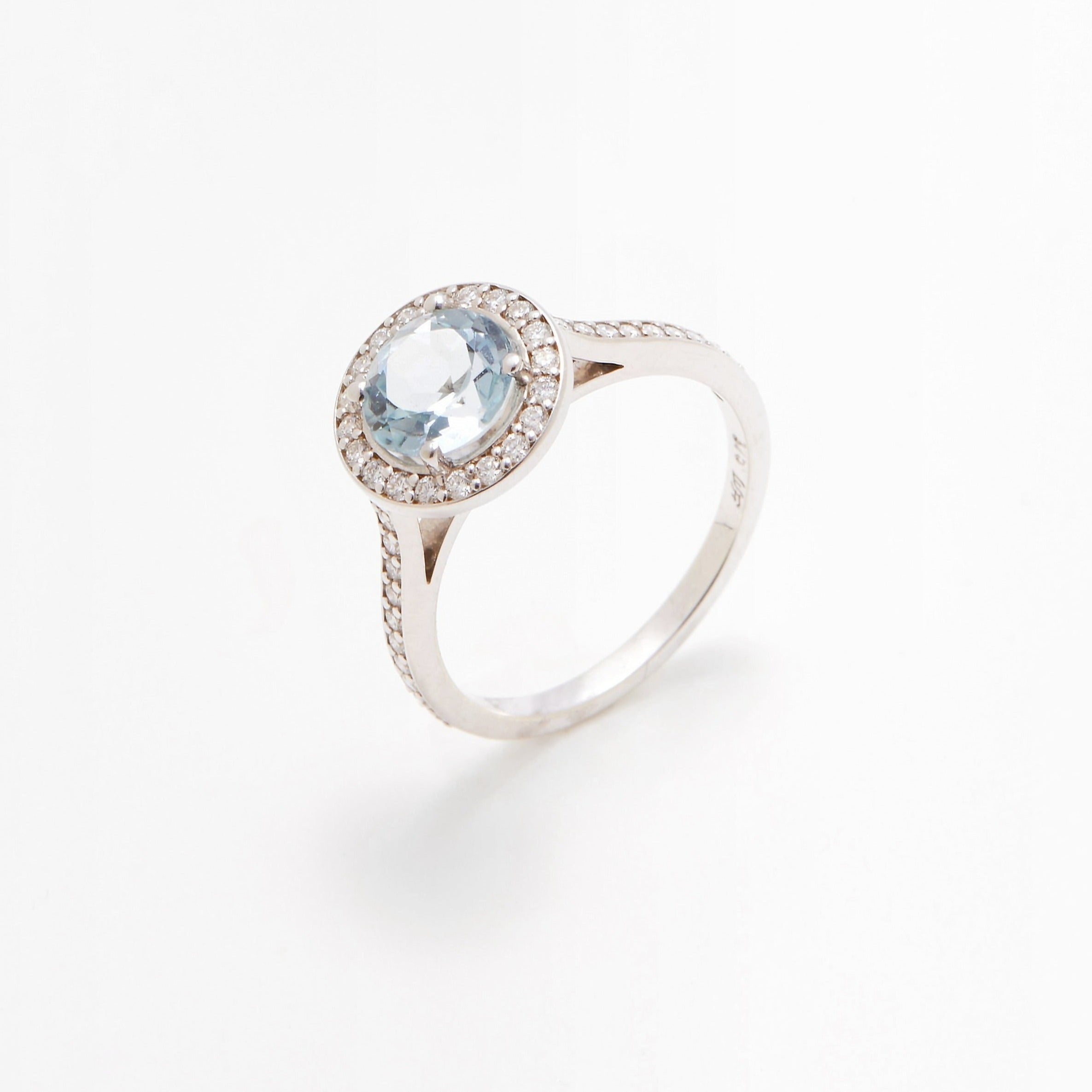 A white gold  halo-style engagement ring with a central blue stone surrounded by white diamonds set in a metal band.