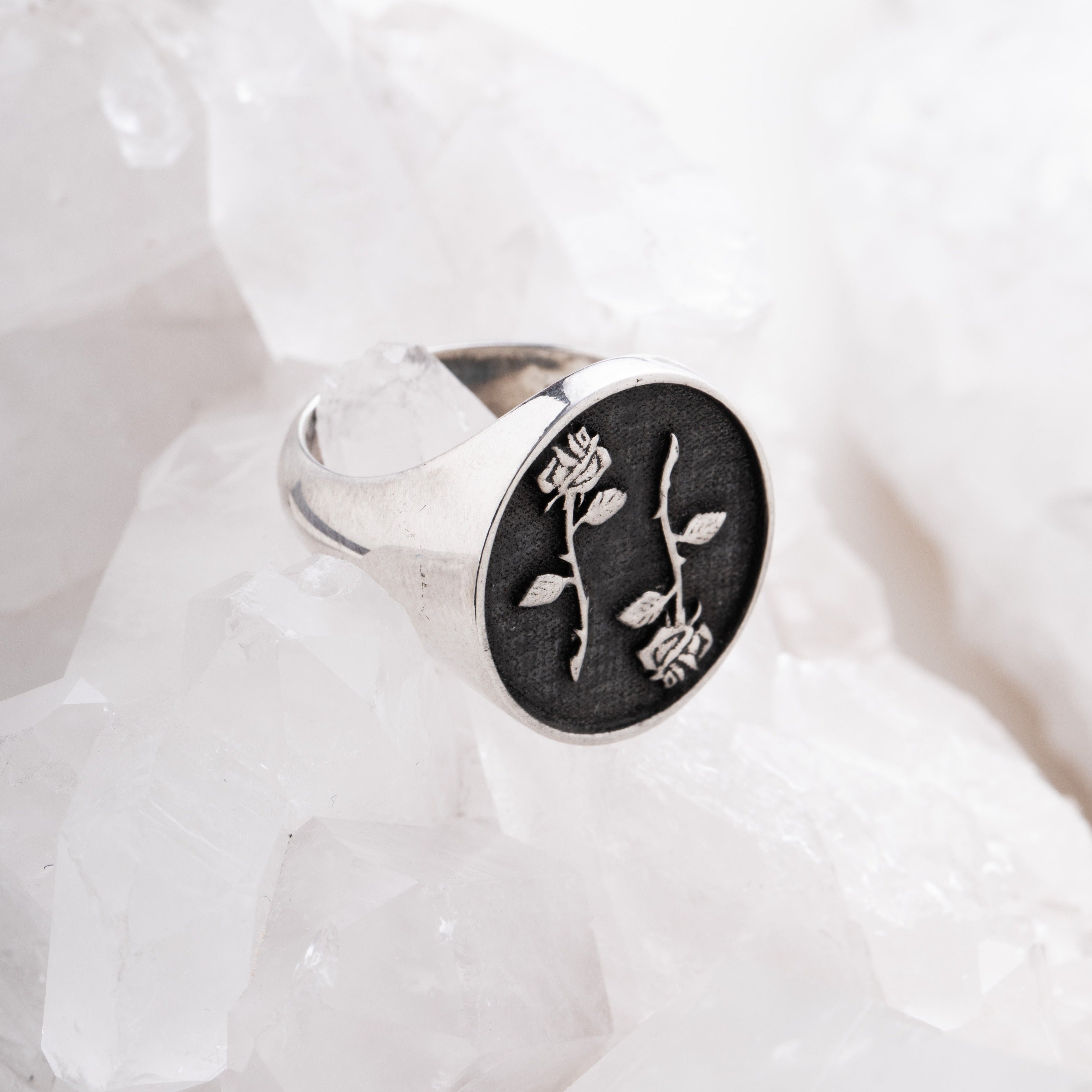 A signet ring with a double-edged rose design on a white background, possibly made of silver or gold, emblematic of the memento mori theme.