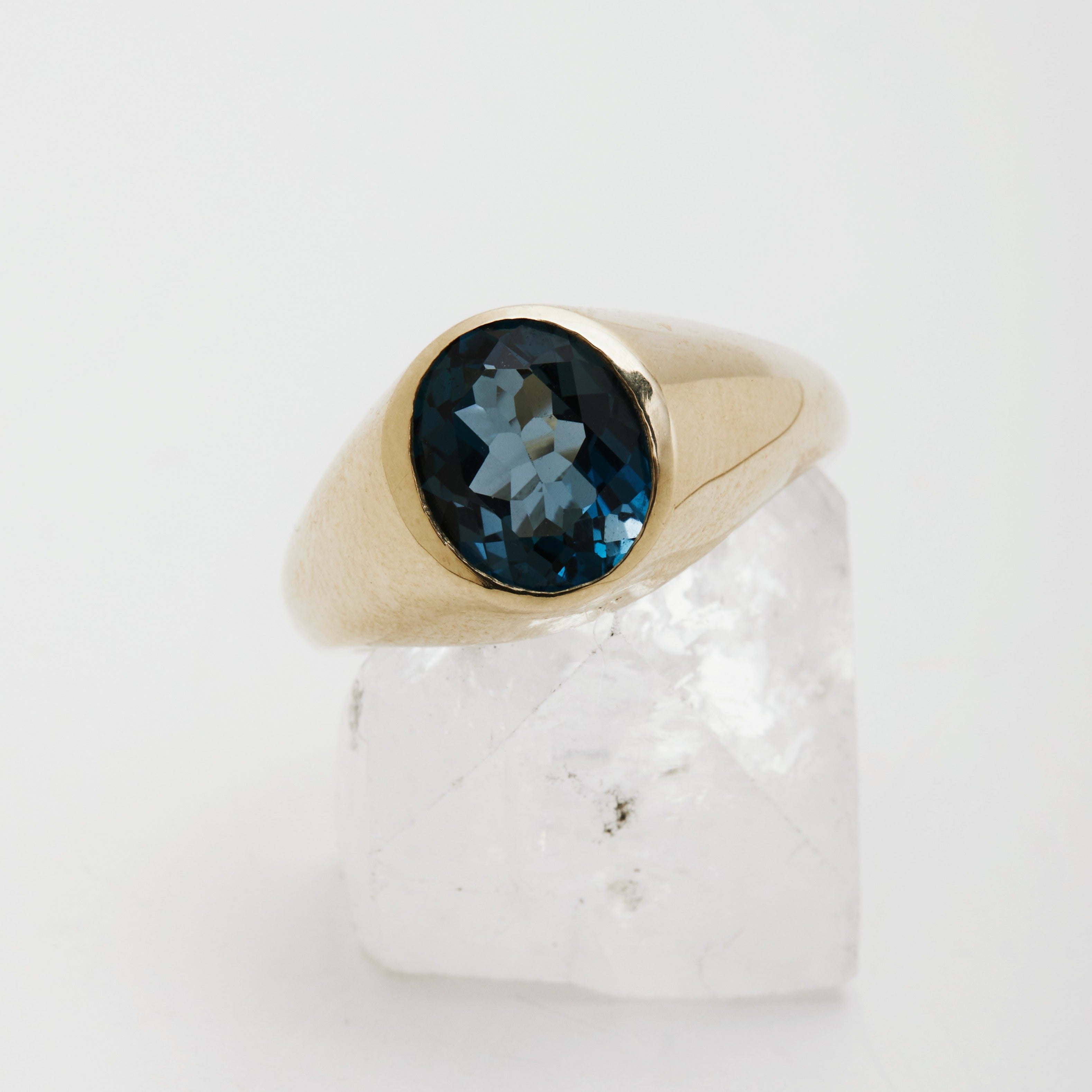 An oval gemstone signet ring set in a gold band, displayed on a white crystal.