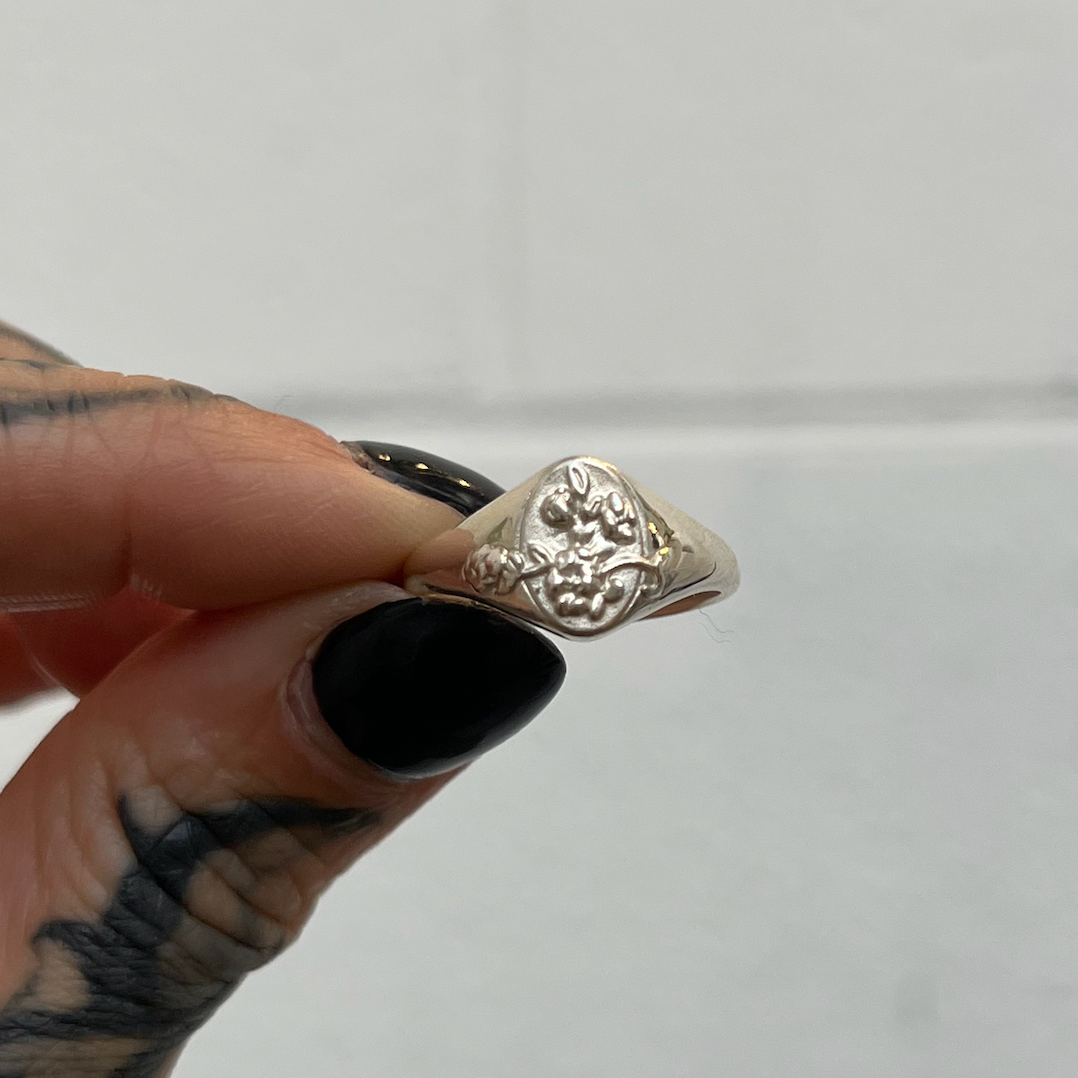 Silver ring held by a hand with black nail polish against a white background