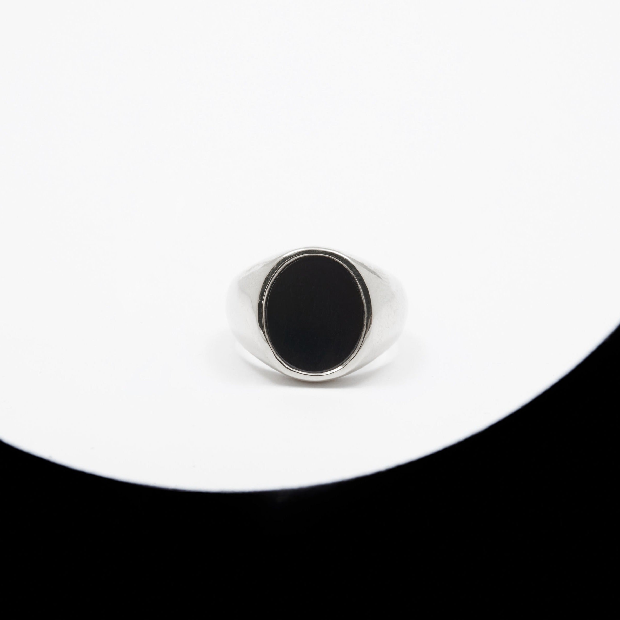 A unisex oval signet ring with a black onyx inlay, made of hollow gold sheet, displayed on a white and black surface.